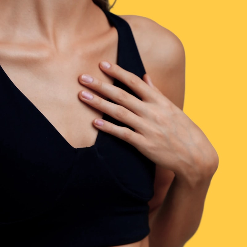 A woman wearing a black top with her hand on her chest, against a yellow background