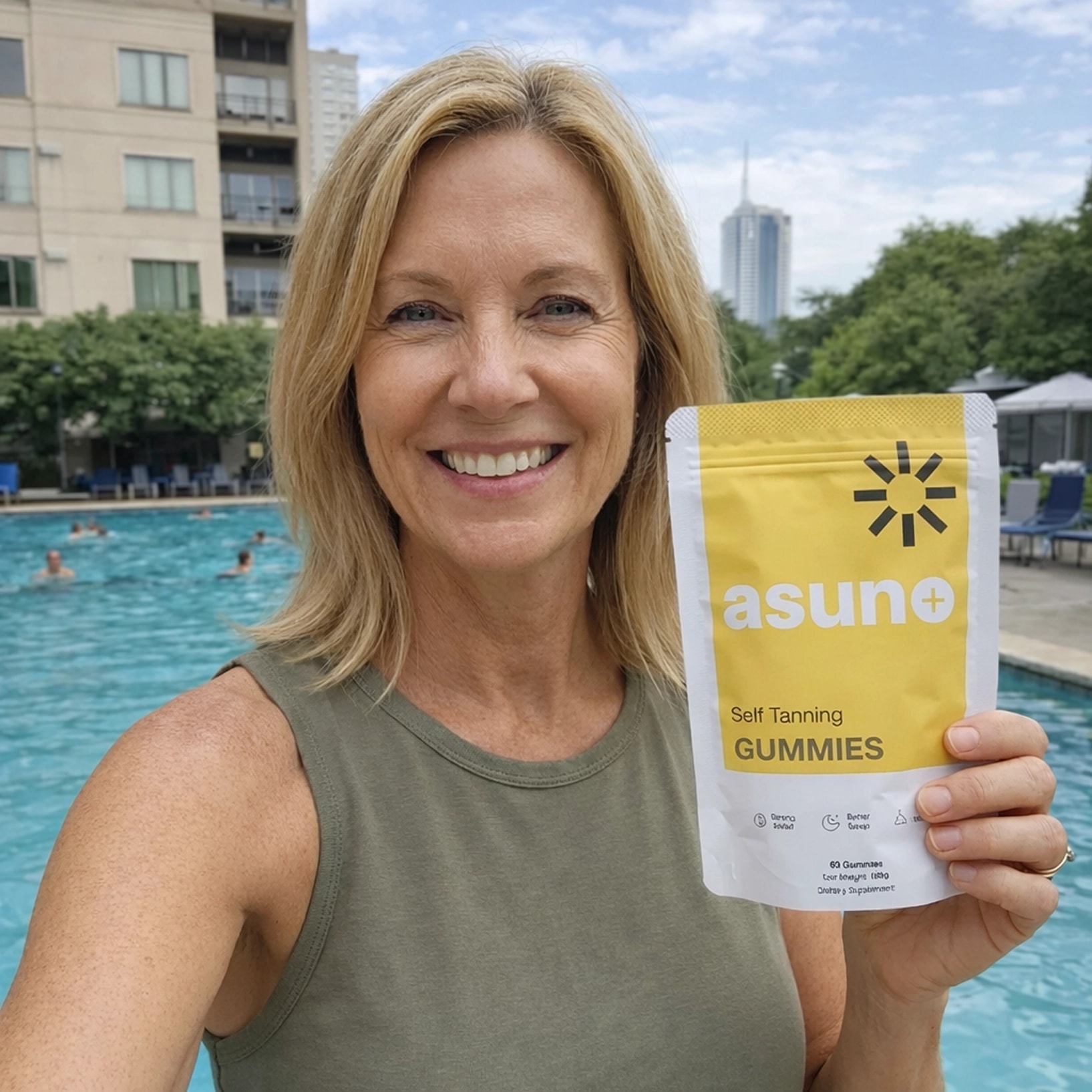 A smiling woman with blonde hair holds up a yellow and white package of Asun+ Self Tanning GUMMIES by a swimming pool with people in the background.
