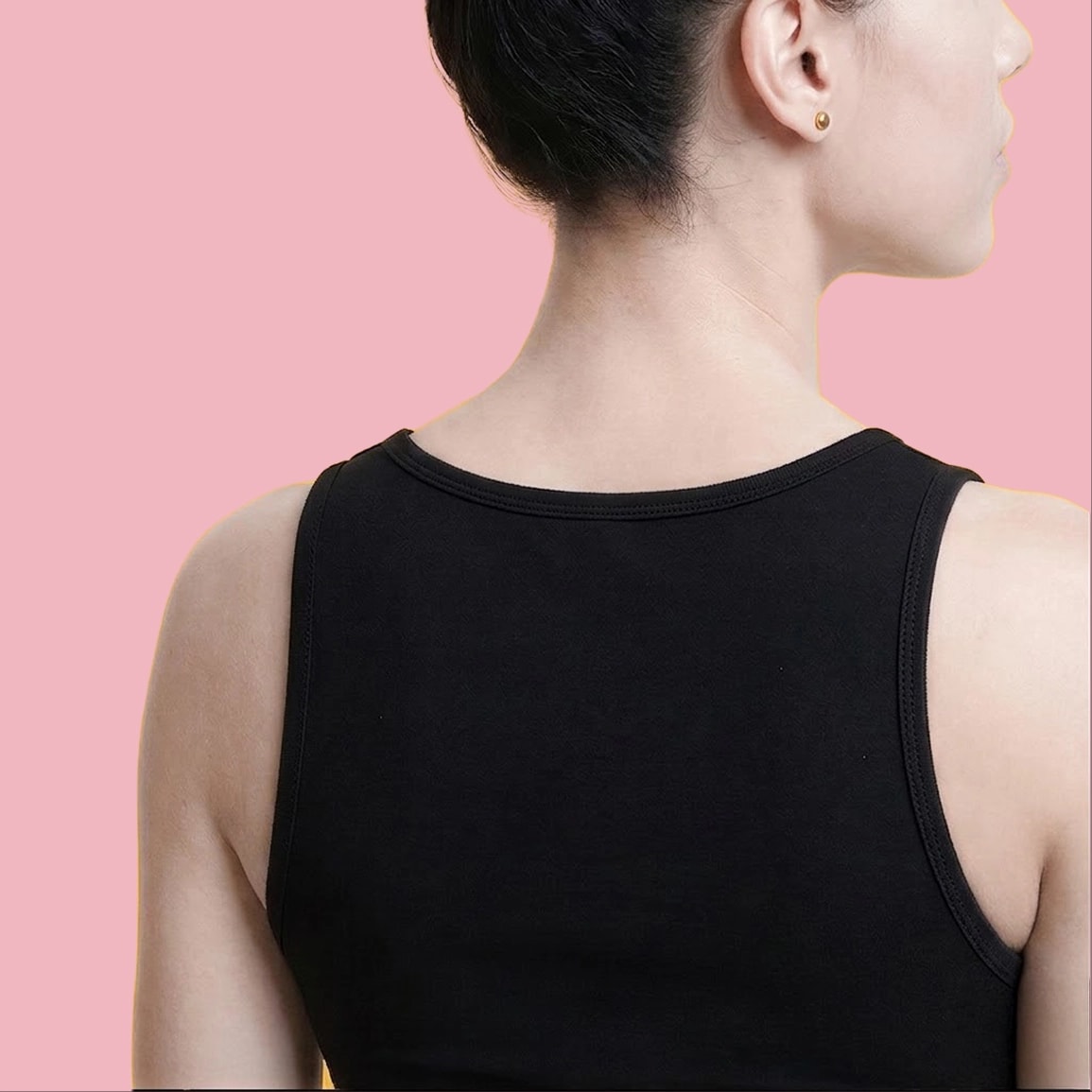 A woman with dark hair pulled back, wearing a black tank top and gold earrings, against a pink background